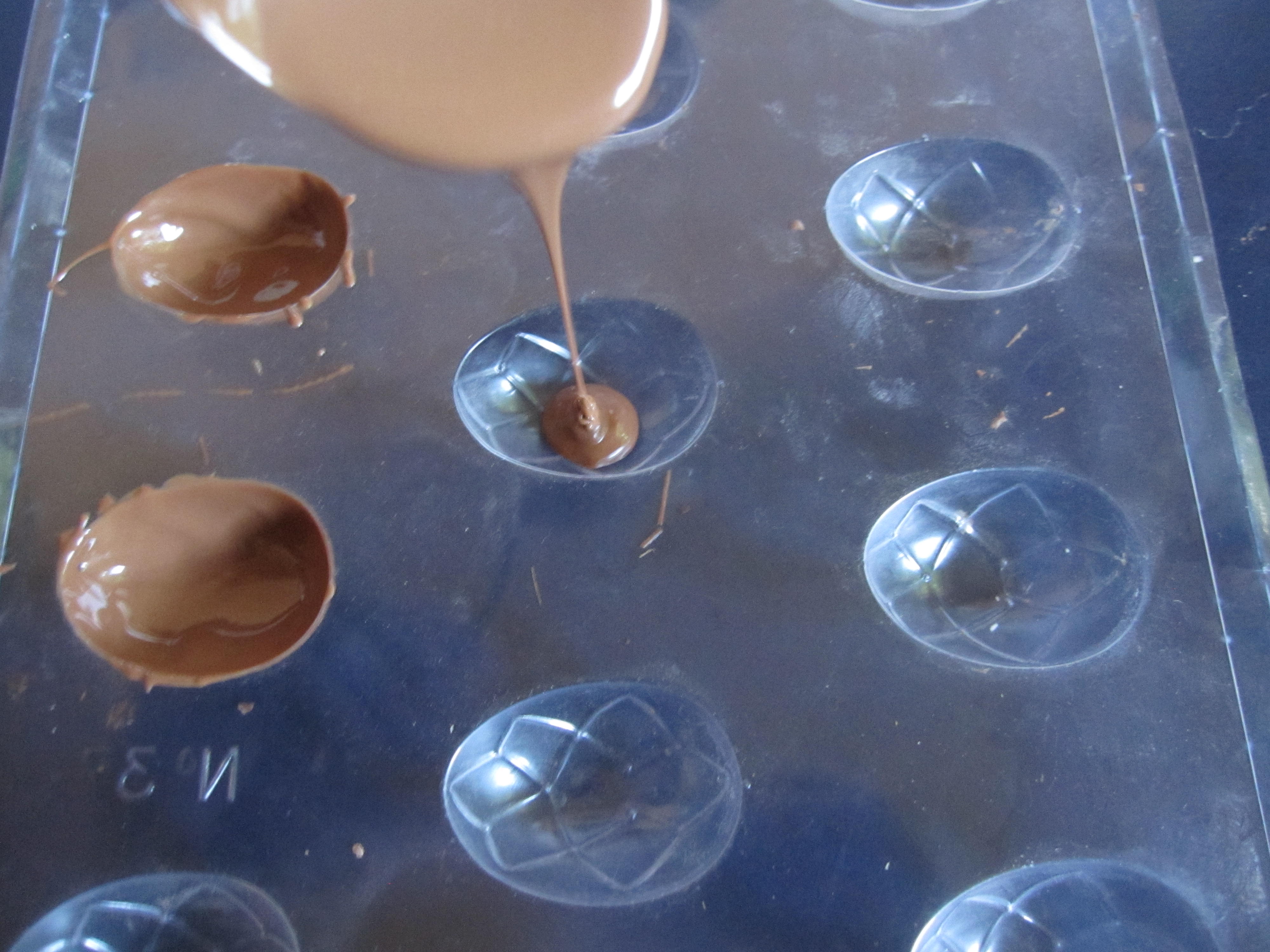 plastic chocolate mould tray with two filled moulds and chocolate pouring from spoon into a third mould